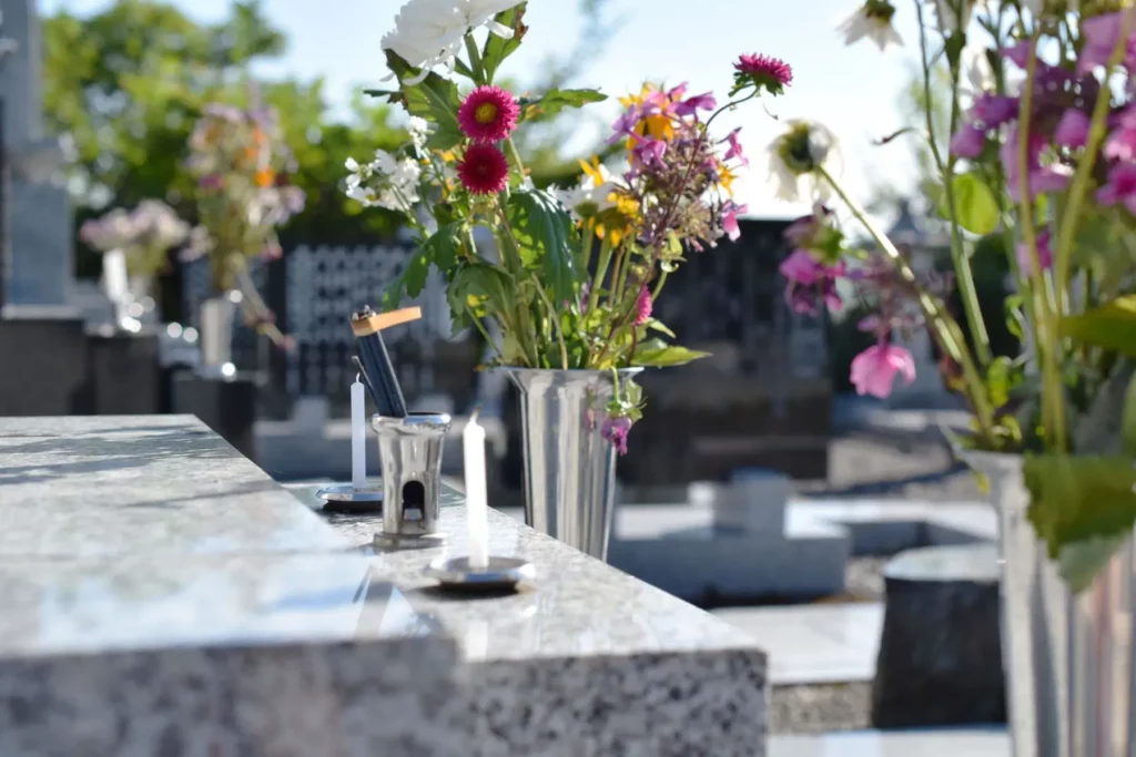 Fleurs fraîches et bougies de recueillement posées sur une pierre tombale.