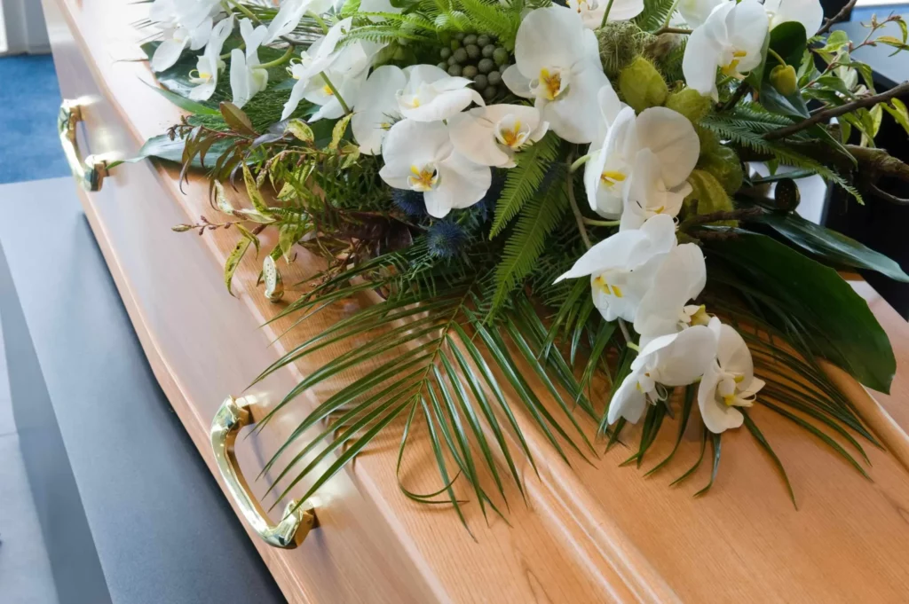 Composition florale avec orchidées blanches déposée sur un cercueil en bois.